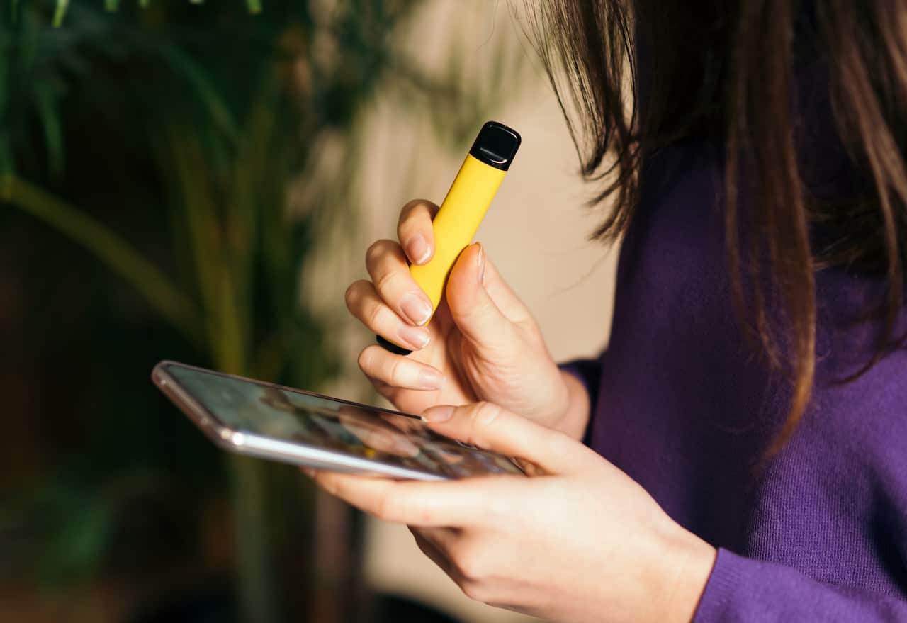 Yellow disposable electronic cigarette in a woman's hand. 