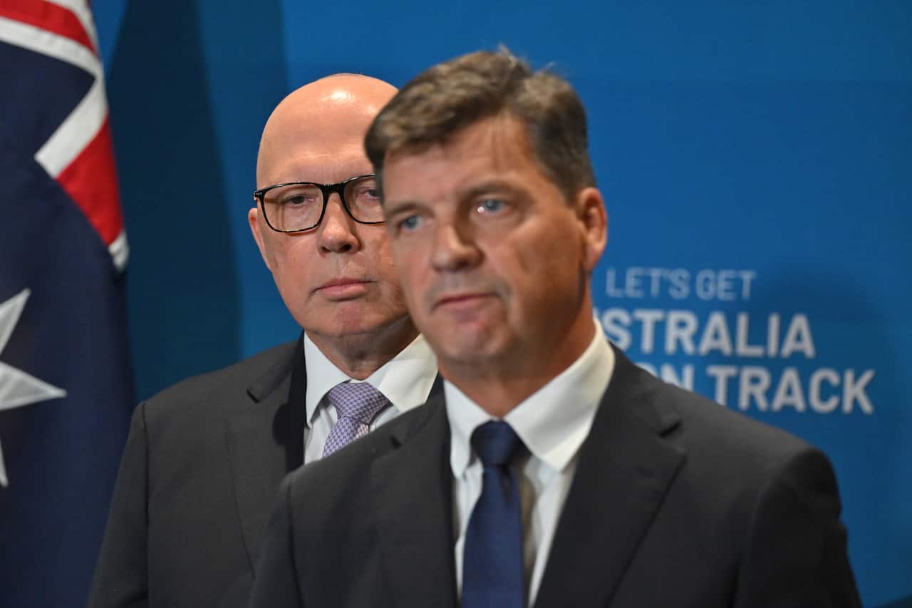 Peter Dutton está atrás de Angus Taylor quando eles aparecem em uma coletiva de imprensa diante de um fundo azul.