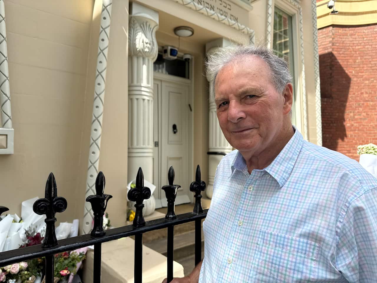 A man in a white chequered shirt stands beside a fence outside a historic building.