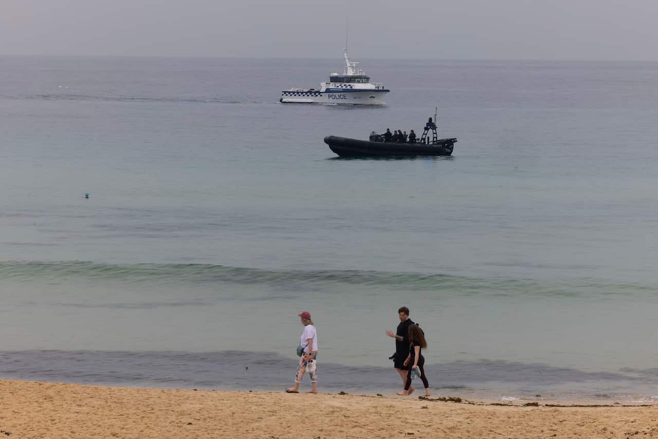 Two police boats on the ocean, in the foreground people walk along a beach 