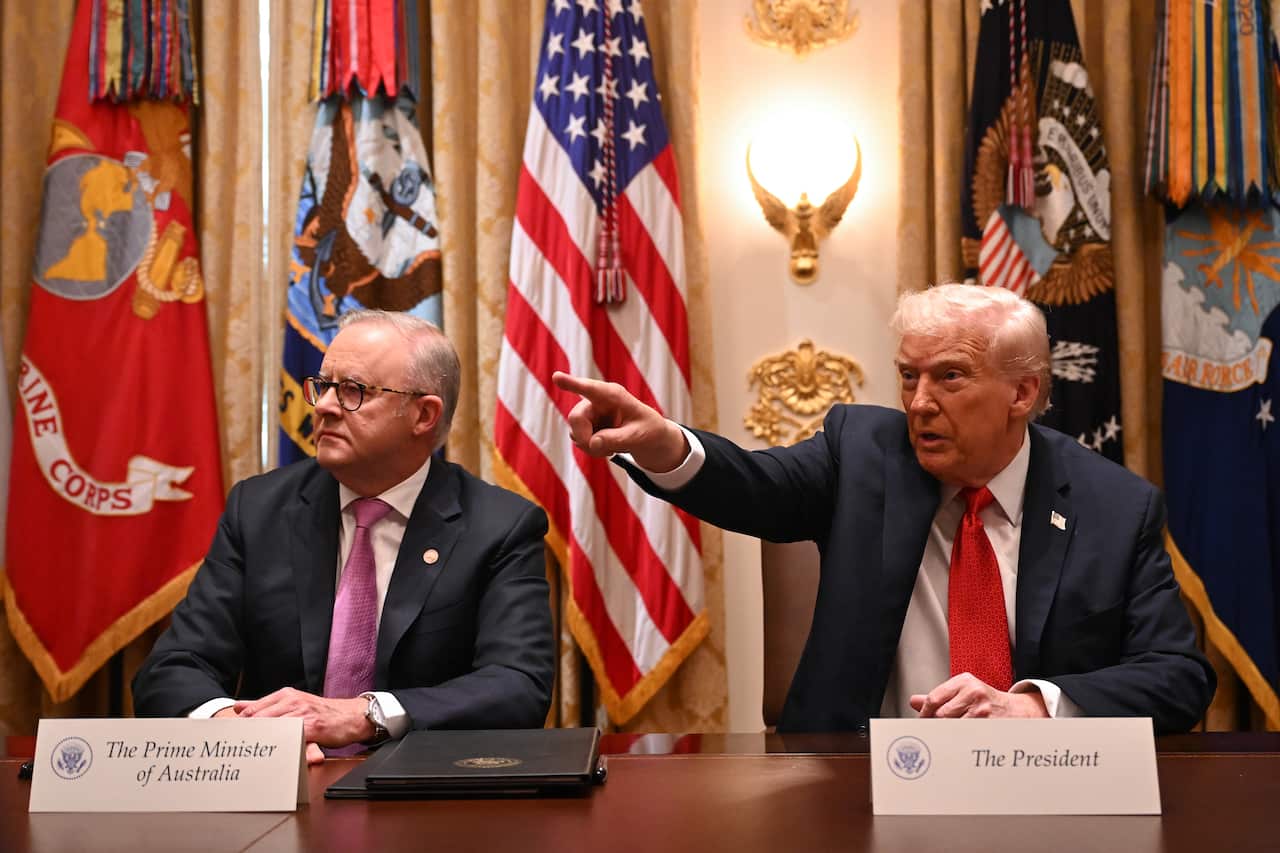Anthony Albanese and Donald Trump are seated beside each other at a table. Trump has his hand pointed out to his right. 