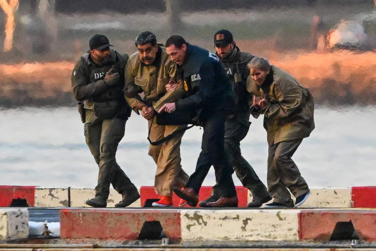 A man and a woman in handcuffs are being escorted by armed officers.