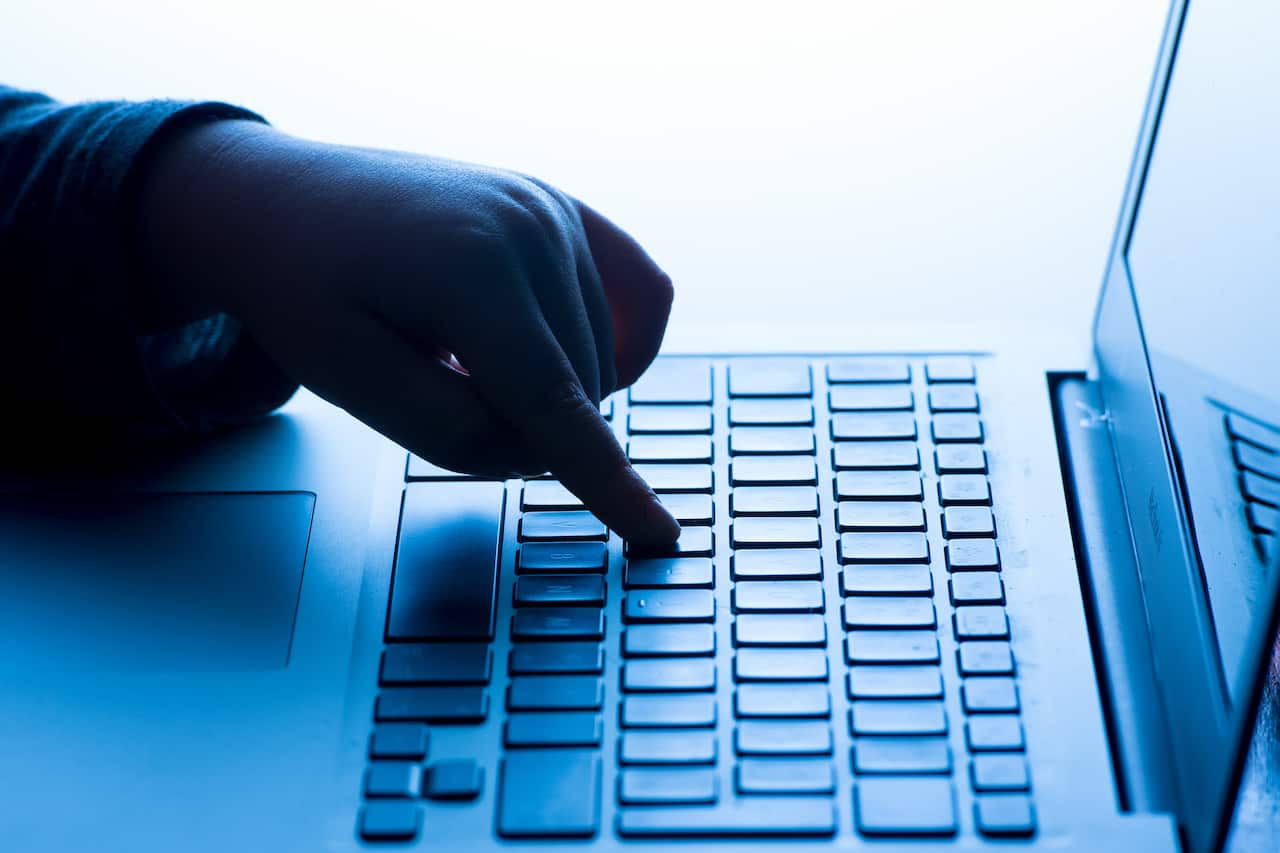 A blue-tinted image shows a person's index finger pressing the key of a laptop