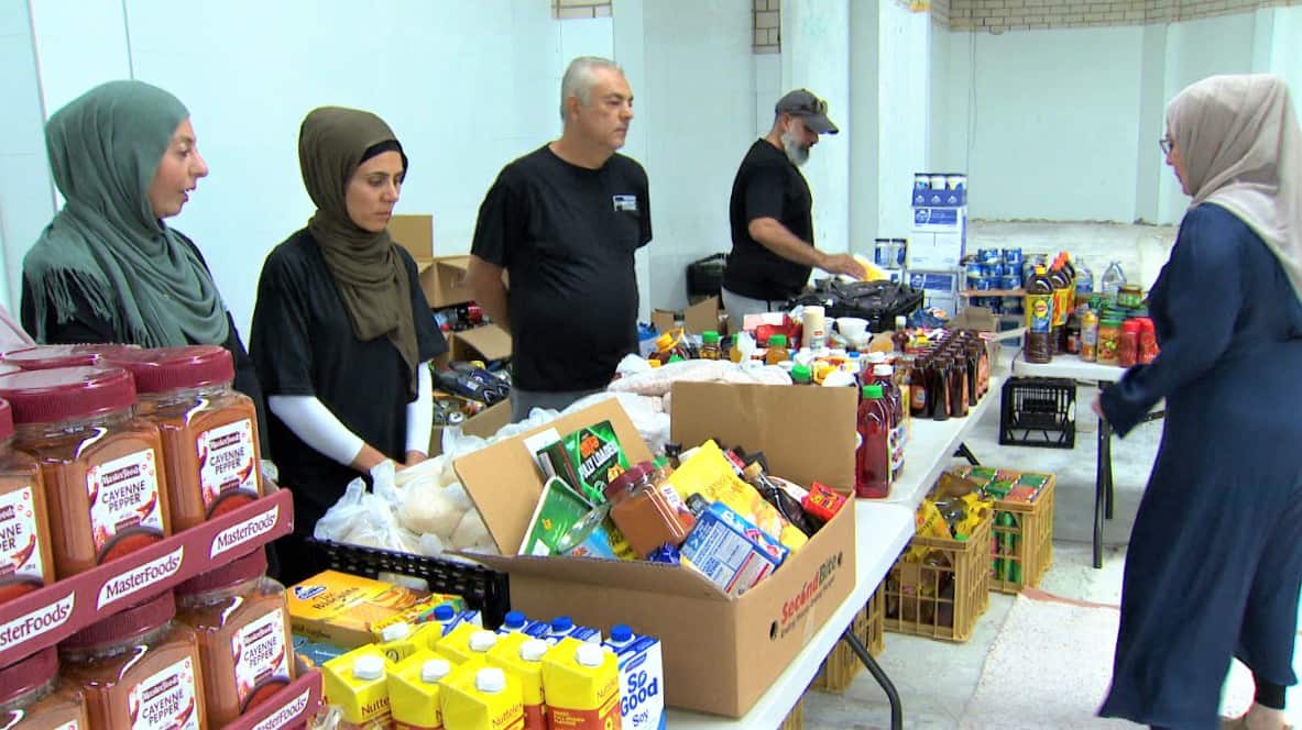 Volunteers stand along a bench laden with food products at a warehouse.