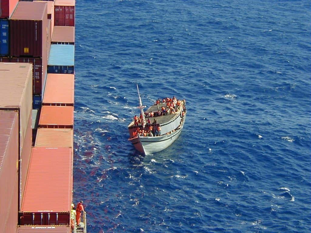 A boat carrying hundreds of people reaches a cargo ship. 