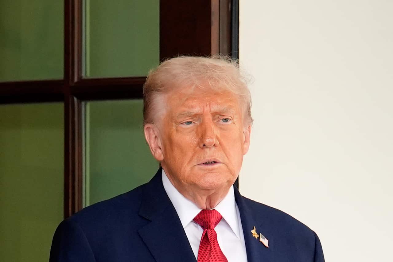 Donald Trump standing in front of a white wall.