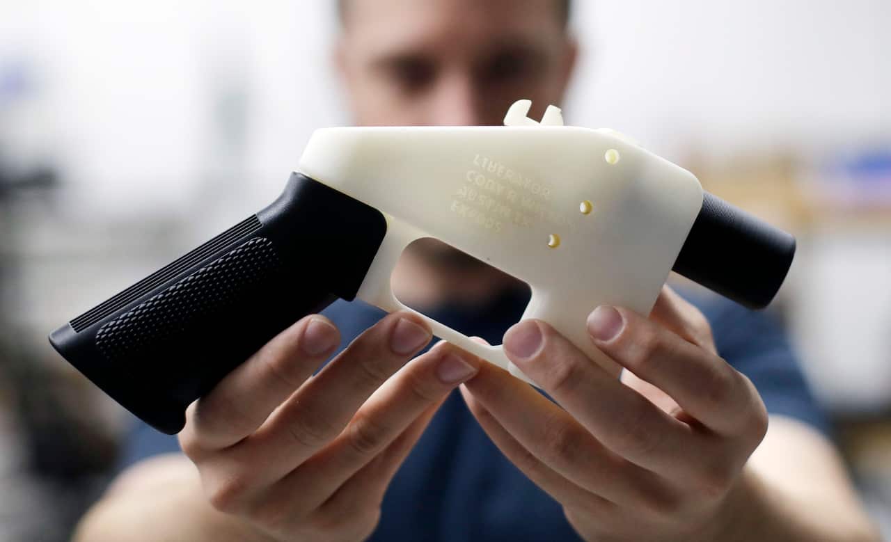 Una persona sostiene una pistola de plástico en blanco y negro que compró una impresora 3D.
