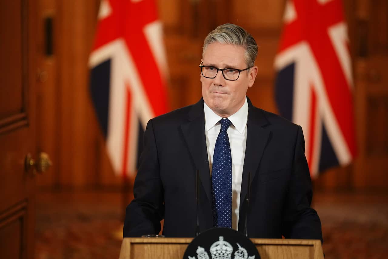 Keir Starmer, standing at a podium in front of two British flags.