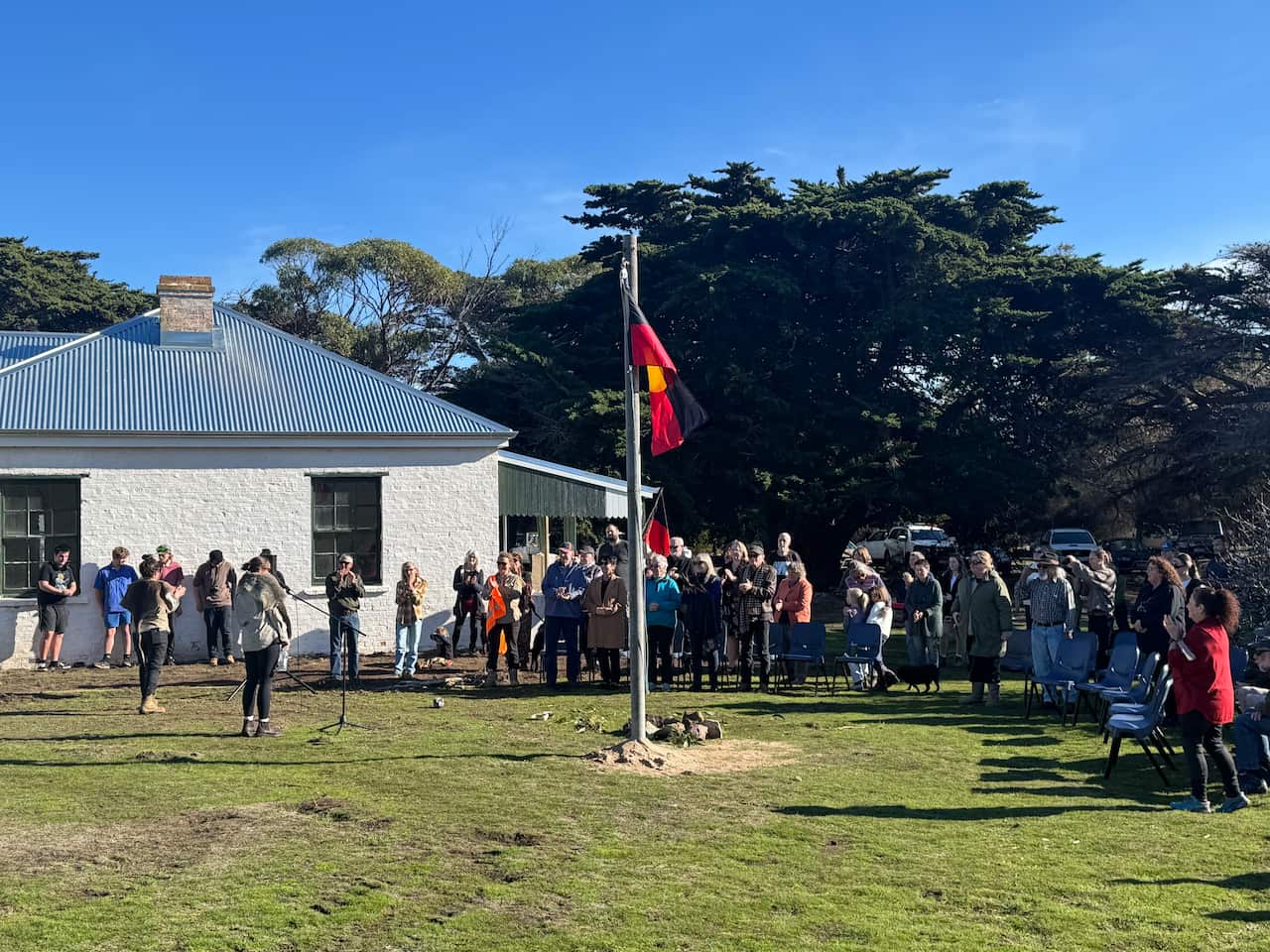Un grupo de personas se reunió alrededor de una bandera aborigen en una asta de asta afuera