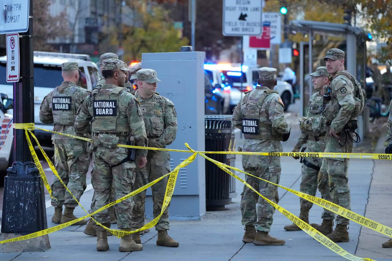 National guard members in camouflage standing near crime scene tape.