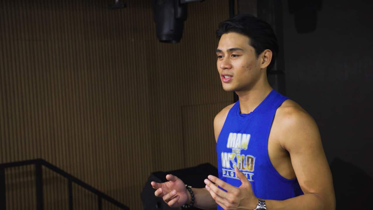 A young Filipino man wearing a blue singlet with "Man of the World pageant" written on it