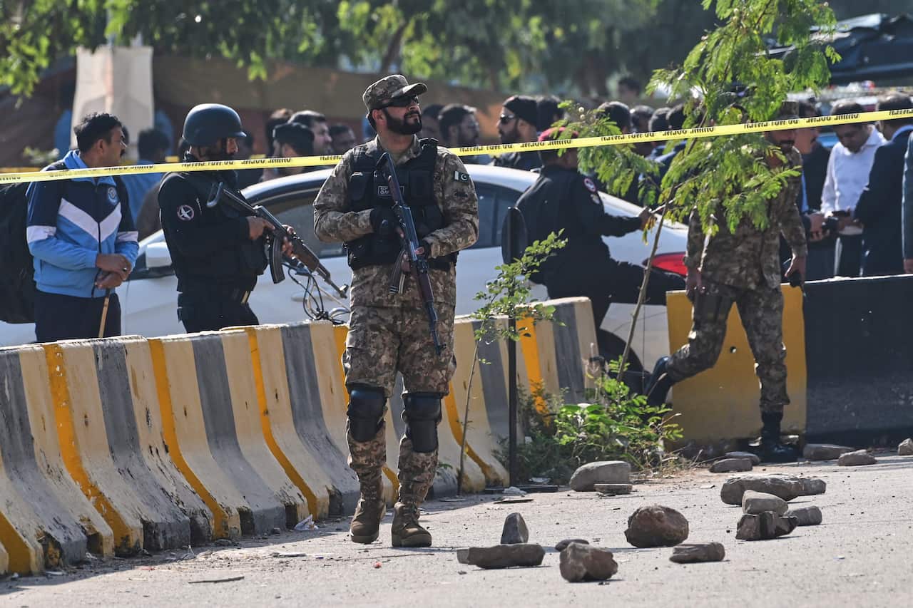 Soldiers walking along the road with police and crowds in backdrop