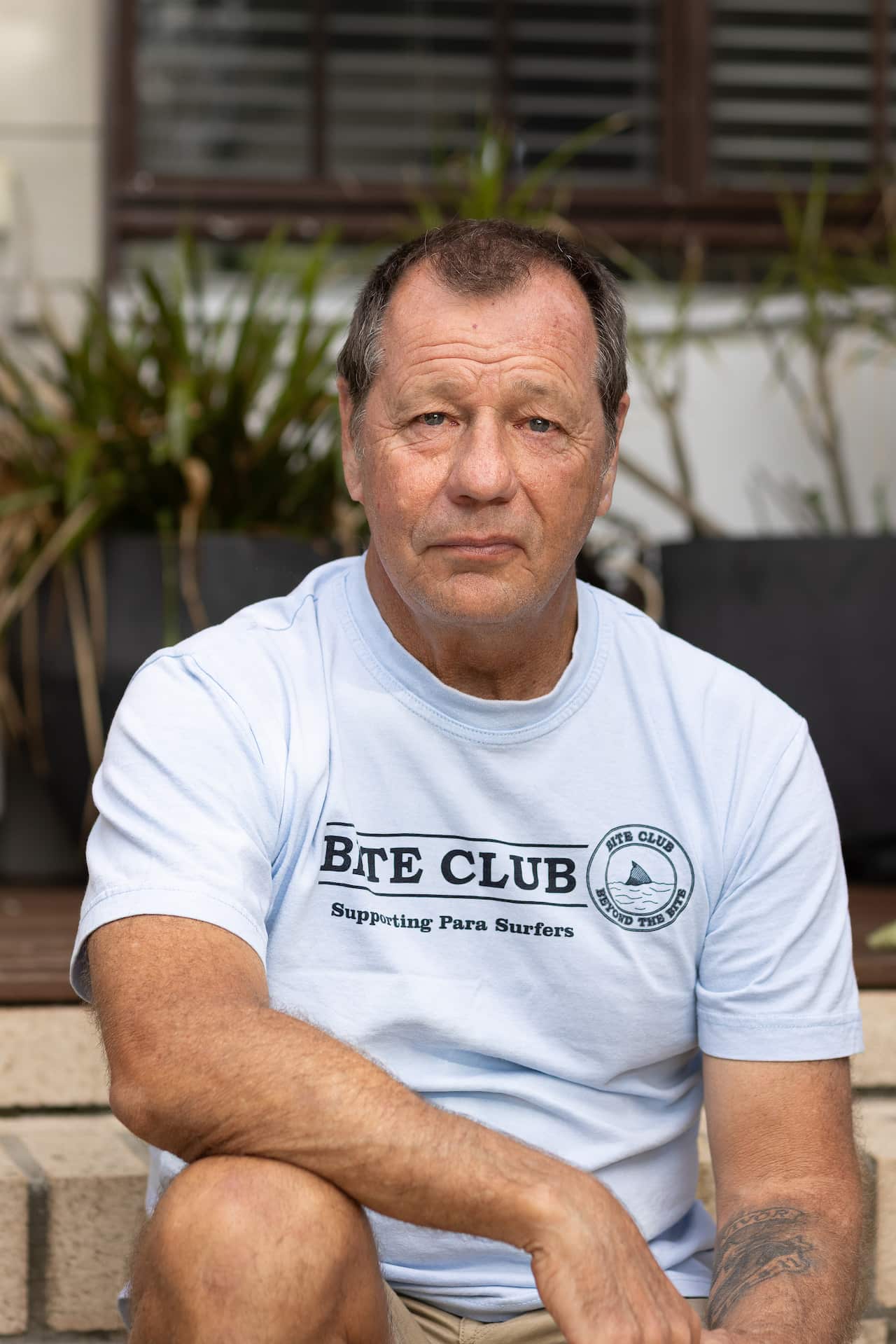 A man wearing a t-shirt saying Bite Club sits wit his right arm resting on his knee.