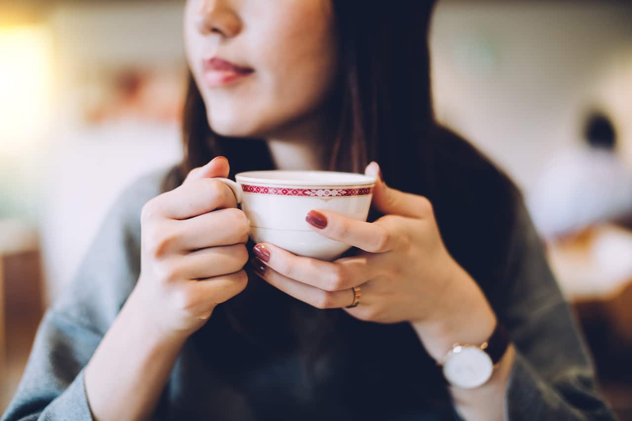 A woman with painted red nails holds a porcelain cup in her hands