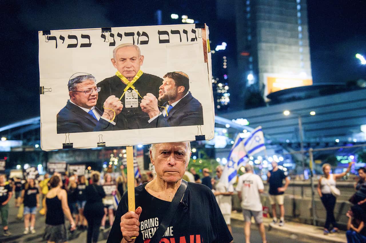 A protester holds up a placard featuring three men. A crowd is visible behind him.