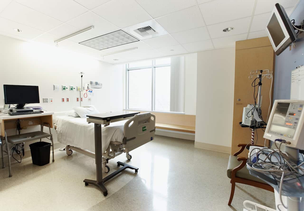 An empty hospital room with a bed, computer and monitors.