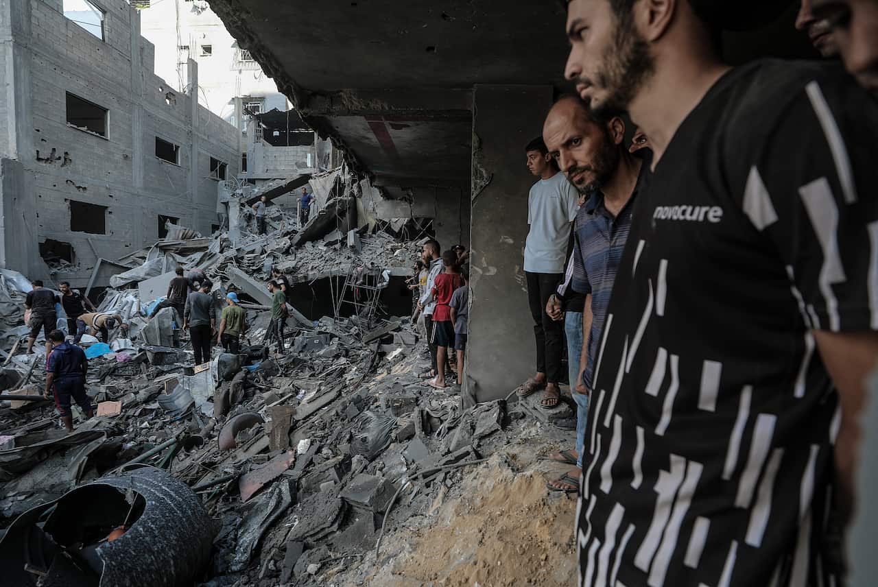 A group of Palestinians standing amidst rubble from heavily damaged buildings.