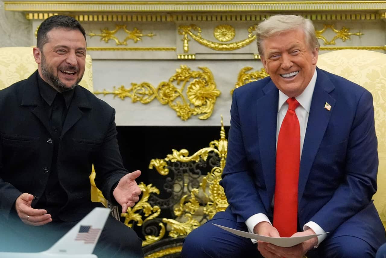 Volodymyr Zelenskyy, in a black suit on the left, and Donald Trump, in a blue suit and a red tie, are sitting next to each other in the Oval Office and laughing during a press conference.