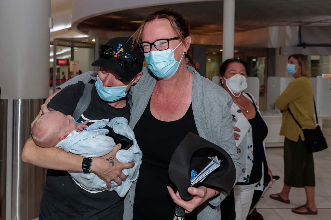 Two people with their arms around each other. One is holding a baby.