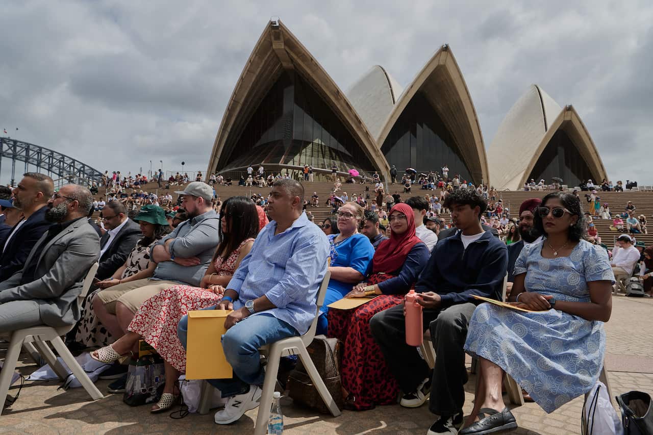 People sitting outside the Sydney Opera House in chairs. The Sydney Harbour Bridge is also visible