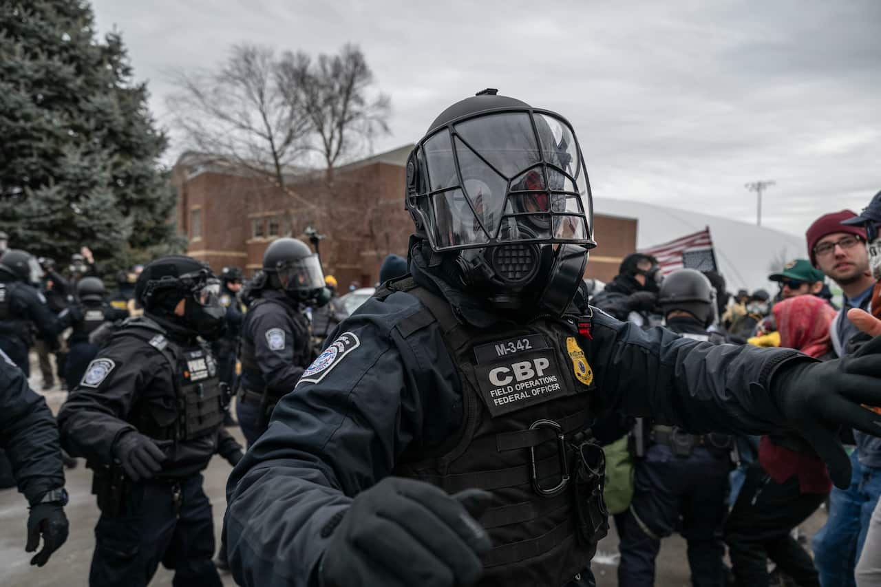 Federal law enforcement officers wearing protective gear attempt to disperse a crowd of demonstrators
