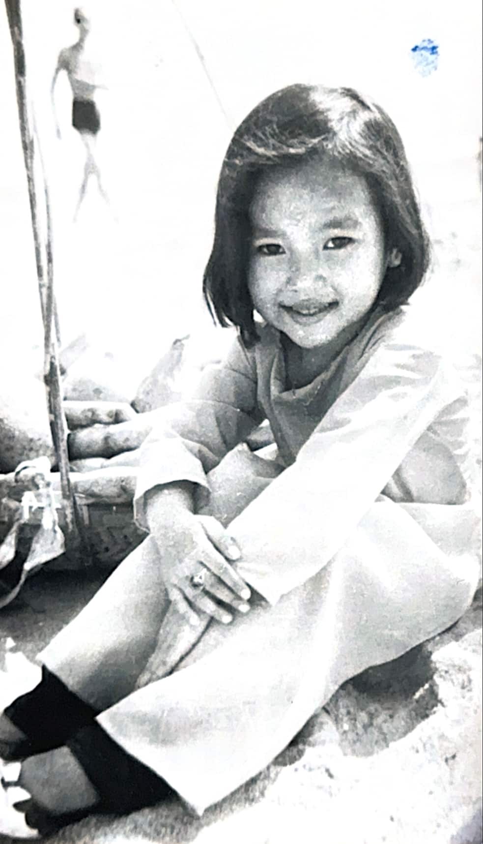 A young girl sits for a photo, with her hands over her knees. 