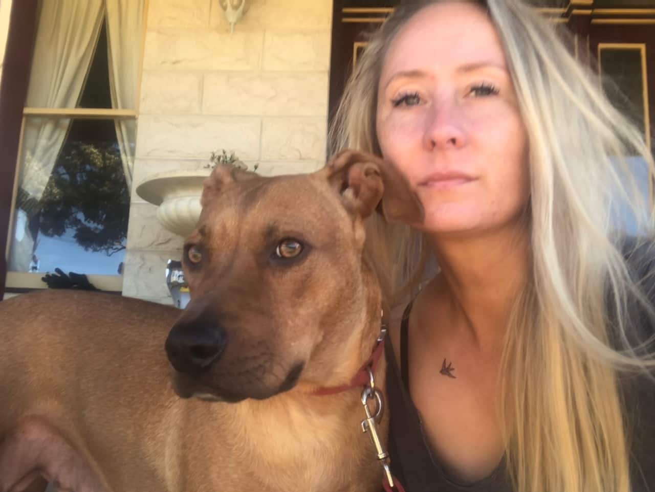 A blonde woman sitting down with a light brown dog next to her.