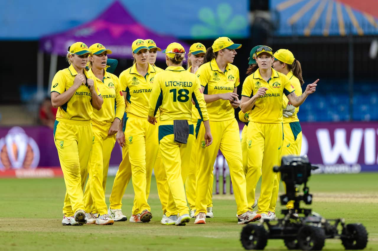 A group of women in yellow and green Australian cricket uniforms walking on a pitch.