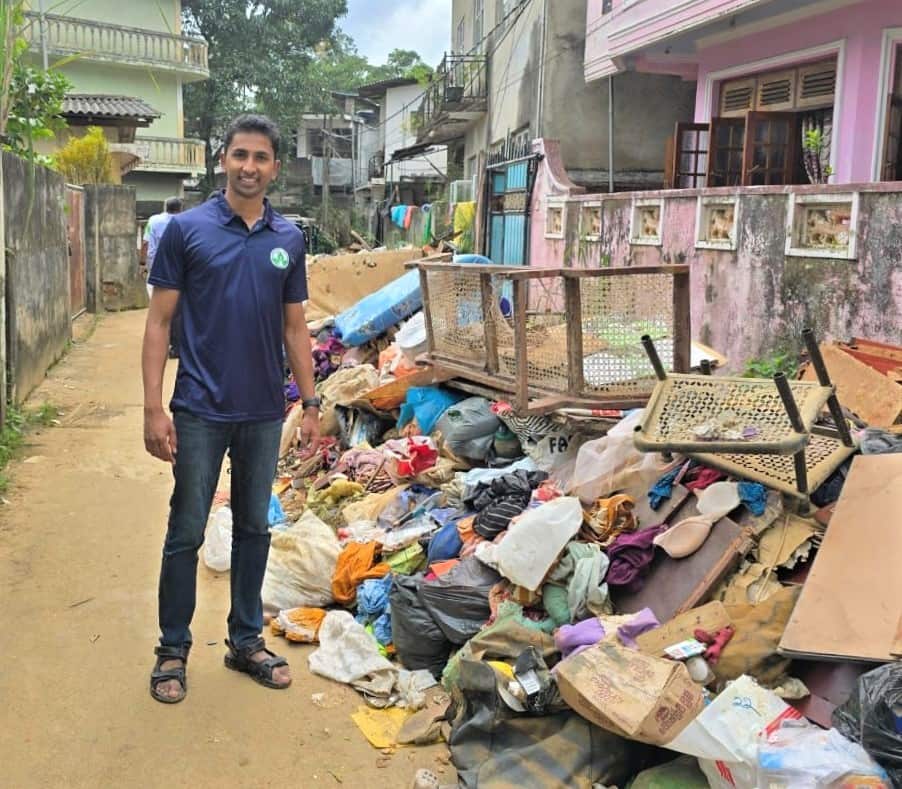 A man in a blue T-shirt stands beside a pile of flood debris.