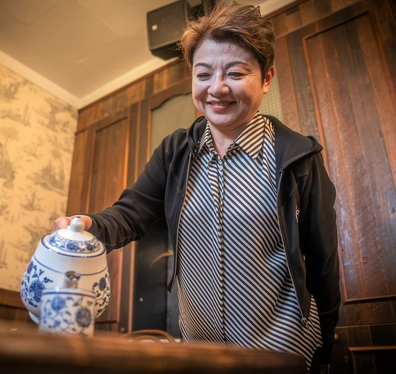 A woman in a striped shirt and black jacket pours tea.