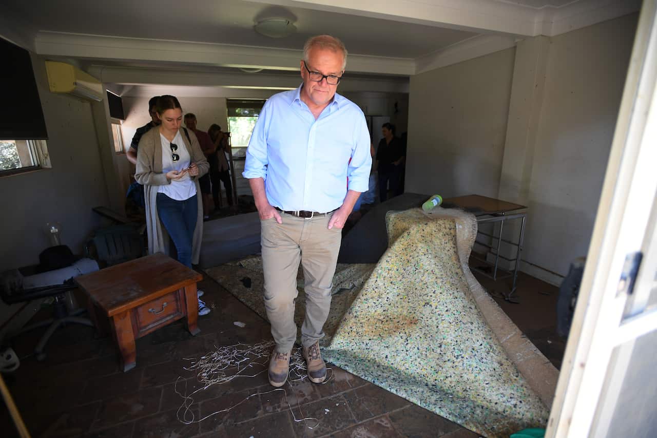 A man in a blue shirt and brown pants looks at a floor in a house.