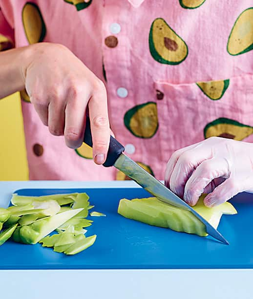 Slicing chokos with gloves on with a knife on a blue cutting board