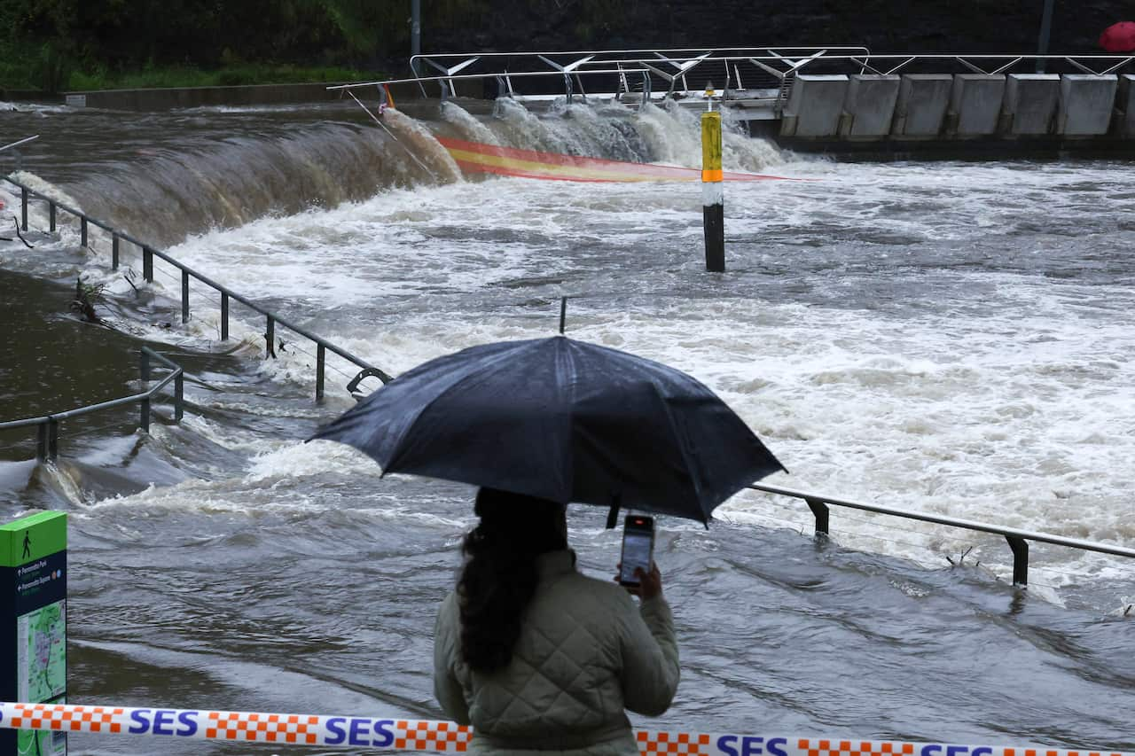 A woman with an umbrella takes a photo of a river overflowing,