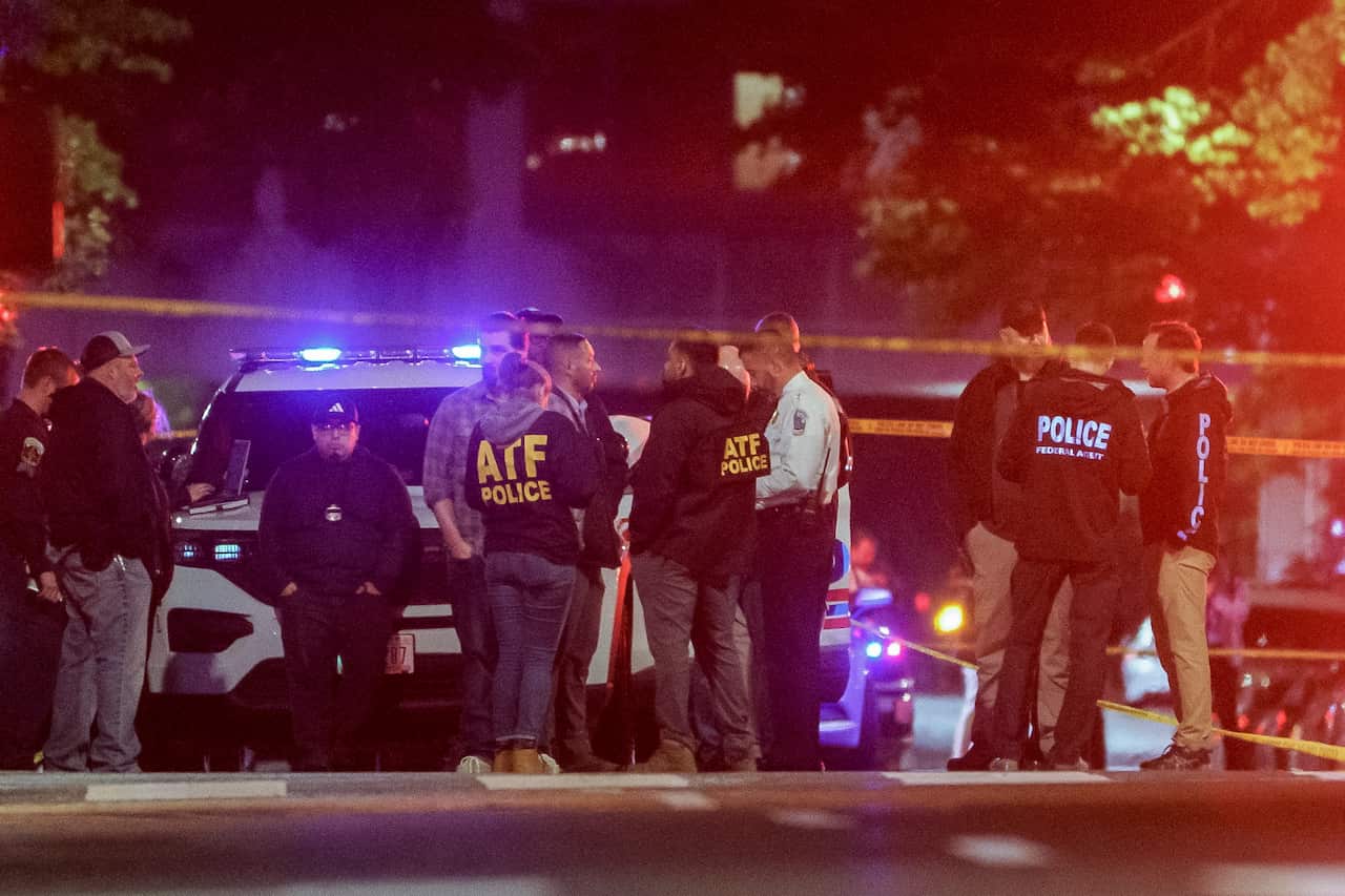 Police officers standing at a crime scene, near yellow police tape.