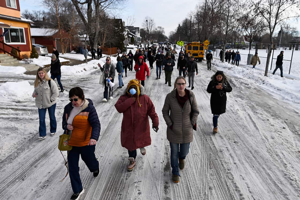 People walking along a snowy and icy residential road. A yellow school bus is parked on one side.