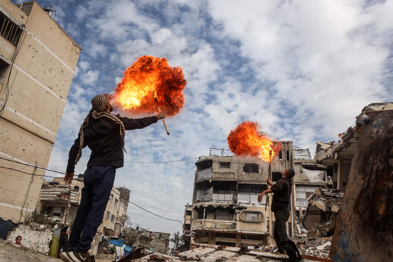 Two men breathing fire surrounded by rubble and destroyed buildings.
