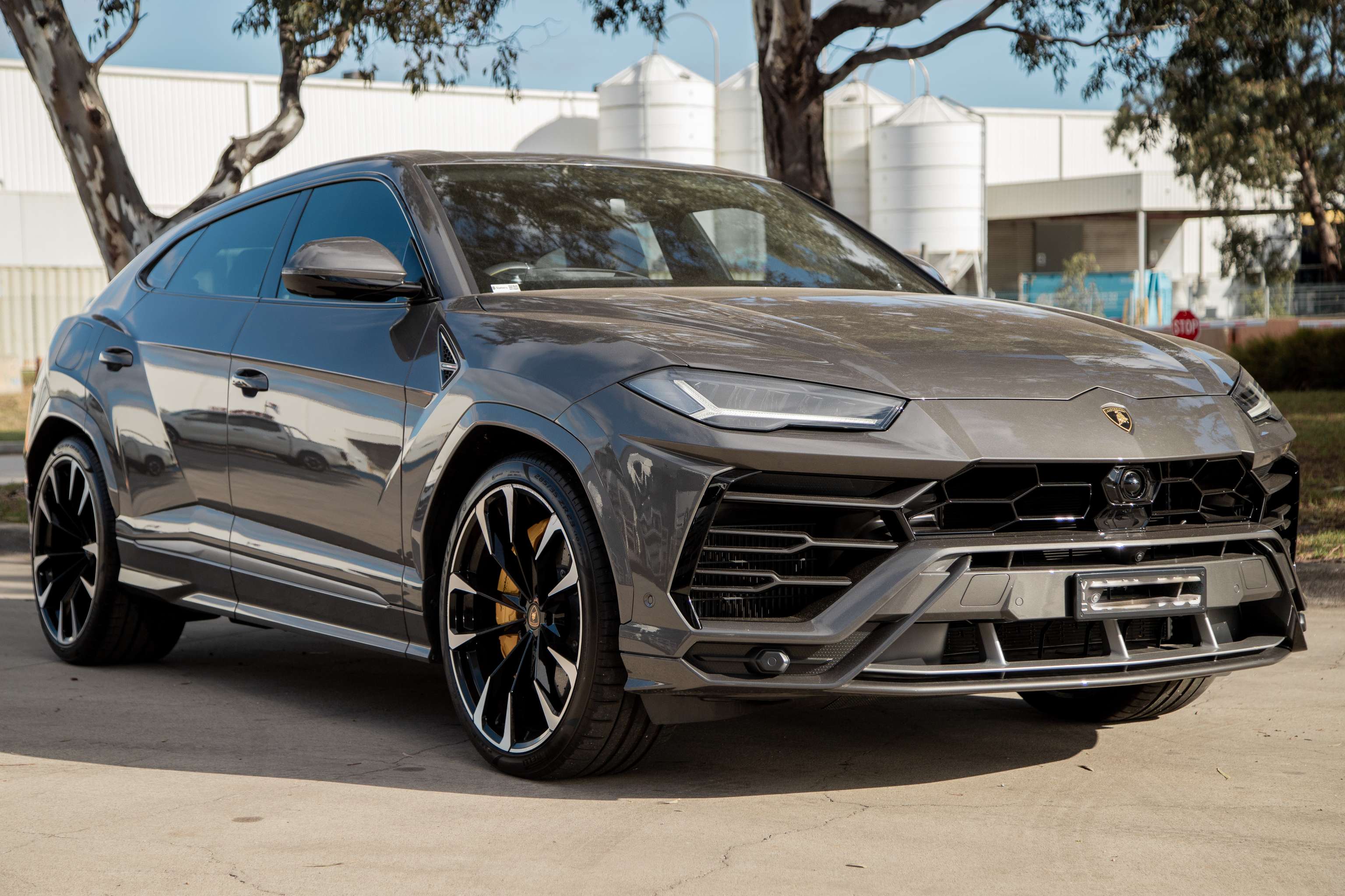 Un SUV Lamborghini gris brillante se encuentra frente a un edificio industrial blanco. 