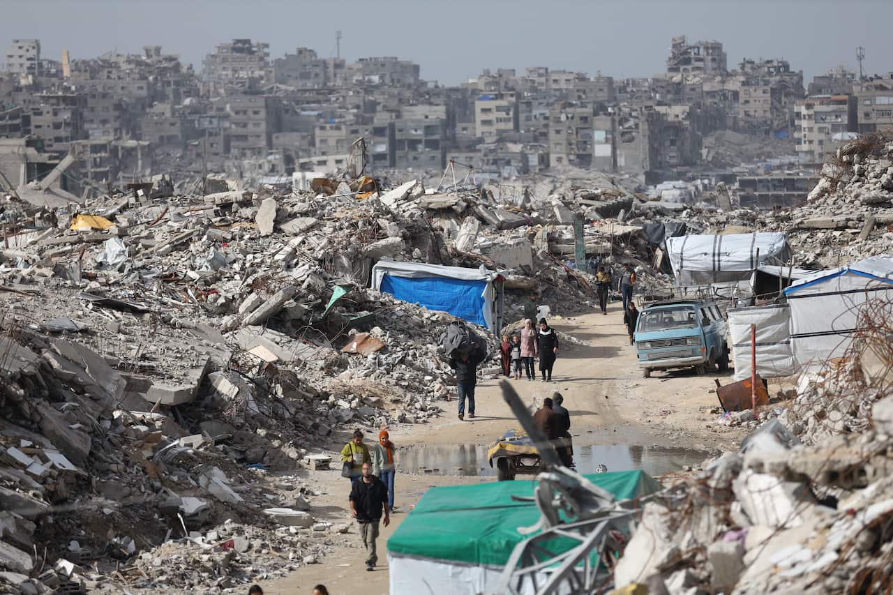 People walking along a dirt road, amid rubble.