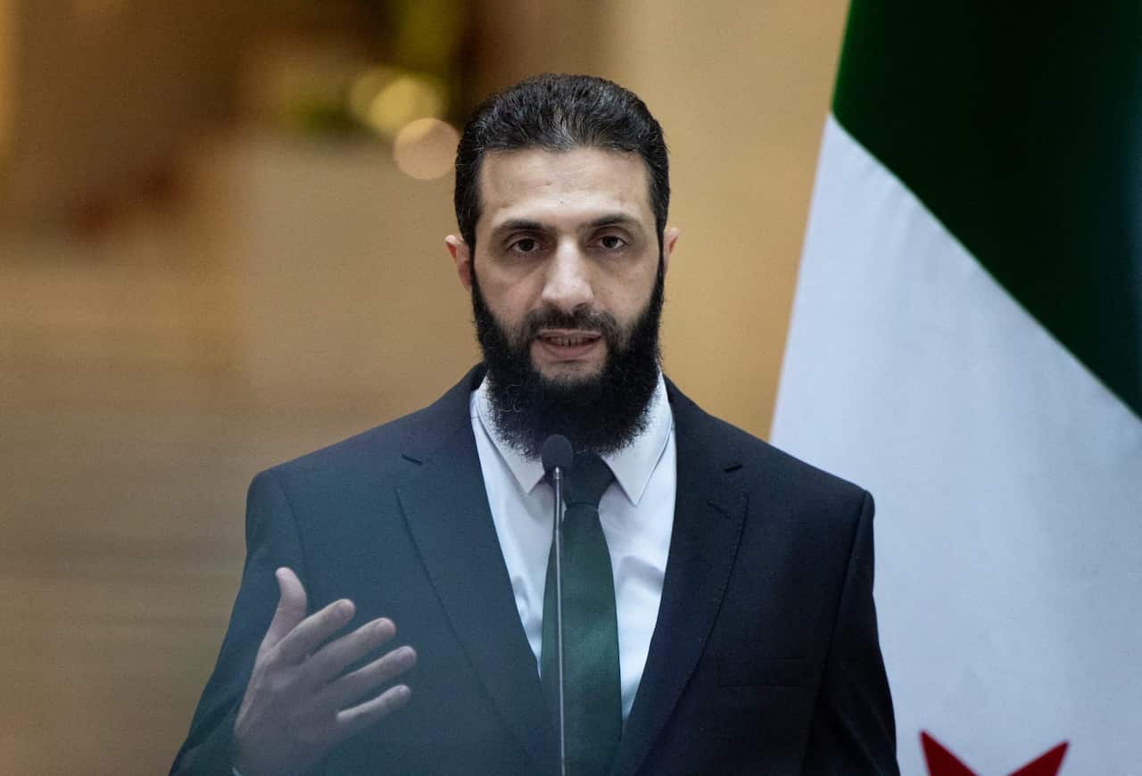 A man wearing a suit and a tie speaks in front of a microphone