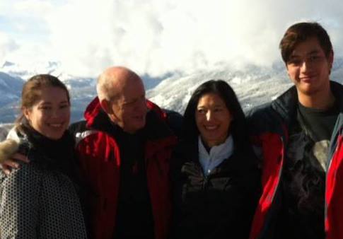 A family of four smiling and posing for a photo, snowy mountains are in the background