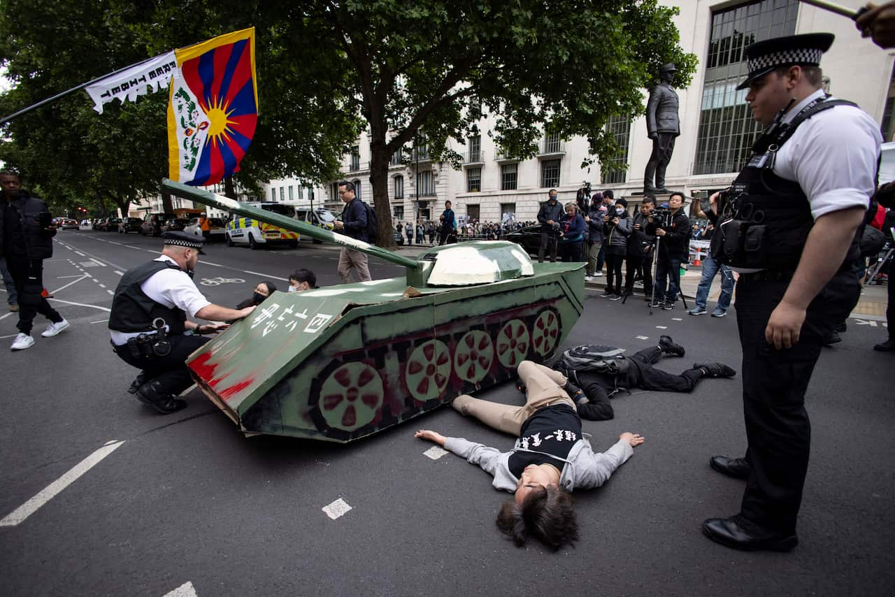 A person lies on the ground near a tank as part of a protest