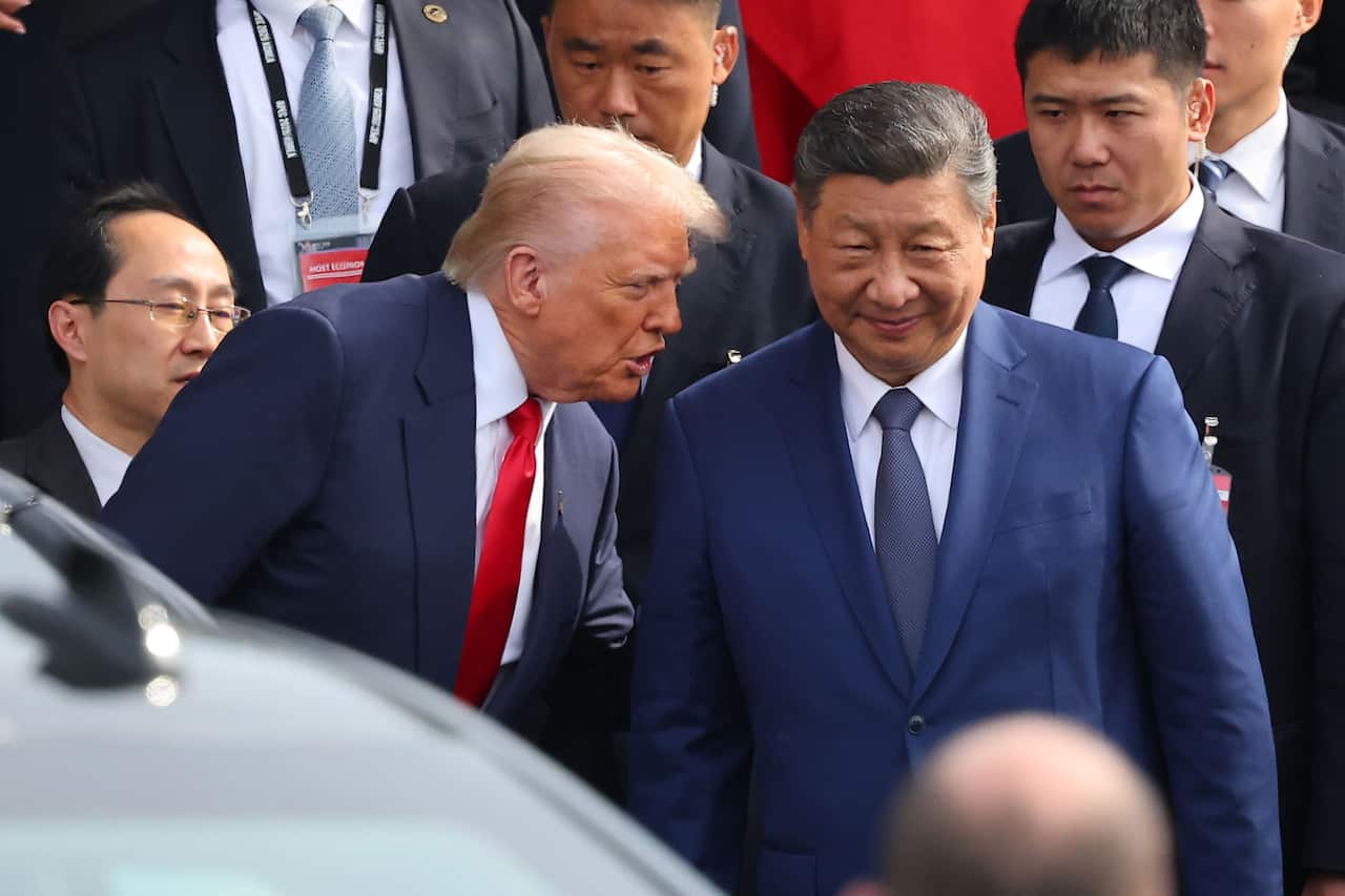 Donald Trump whispering to Xi Jinping. They are surrounded by several men in suits.