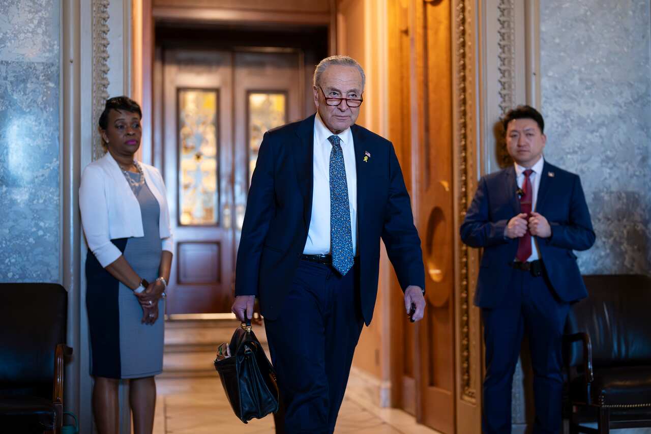 A man in a dark suit walks through heavy, wooden doors holding a briefcase.