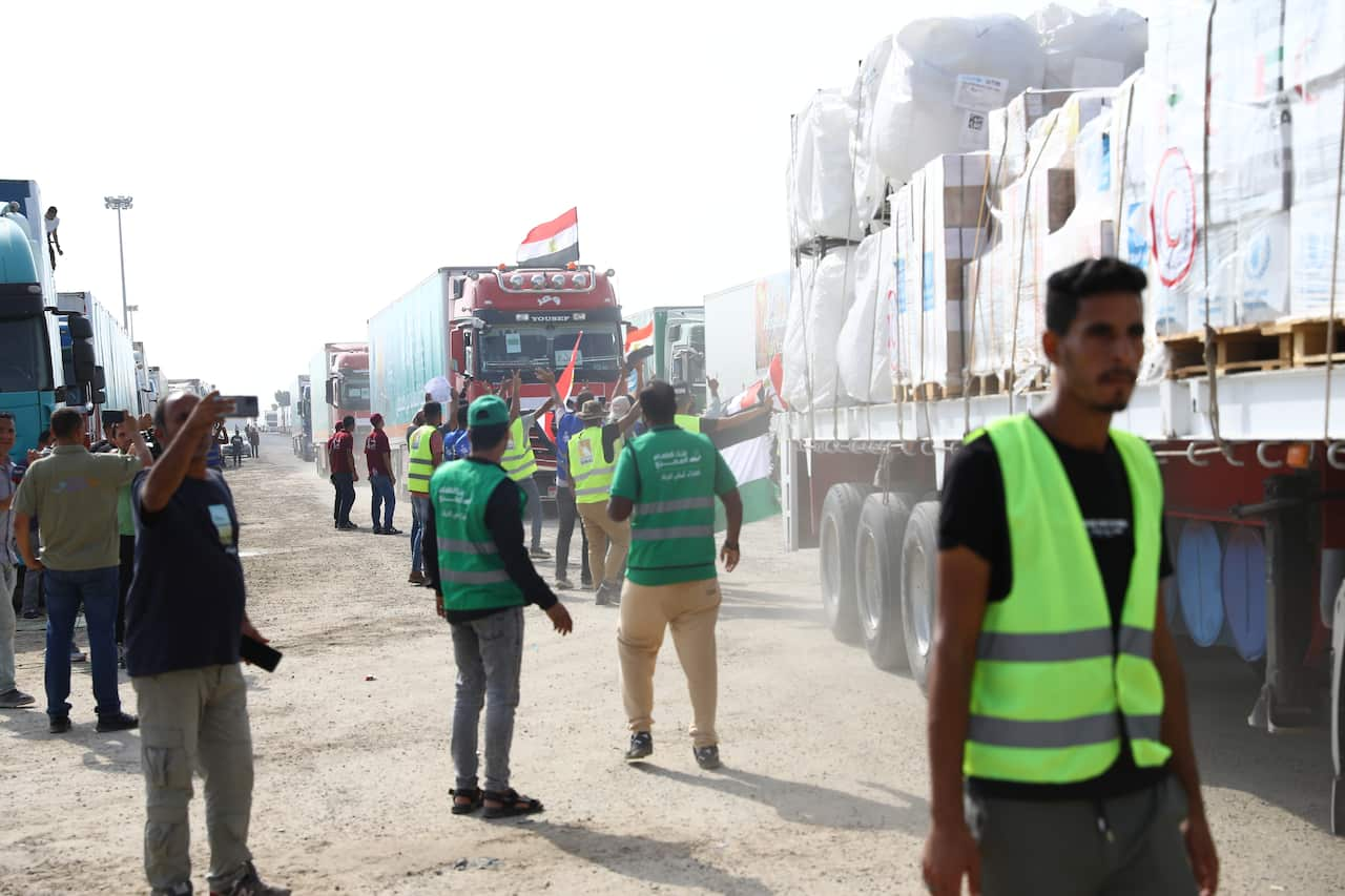 People in fluorescent vests walk alongside aid trucks lining up along dirt road