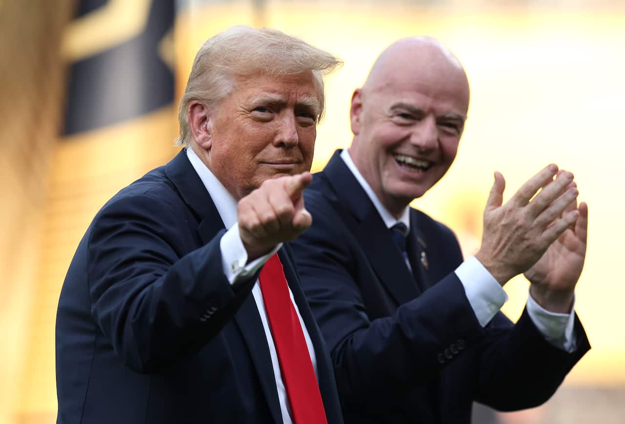 Donald Trump points at camera with Gianni Infantino applauding next to him.