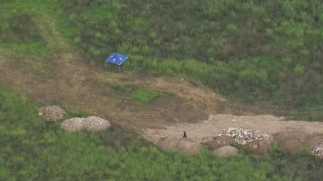 An aerial view of a green paddock. A blue marquee is set up and a person is walking along a dirt track.