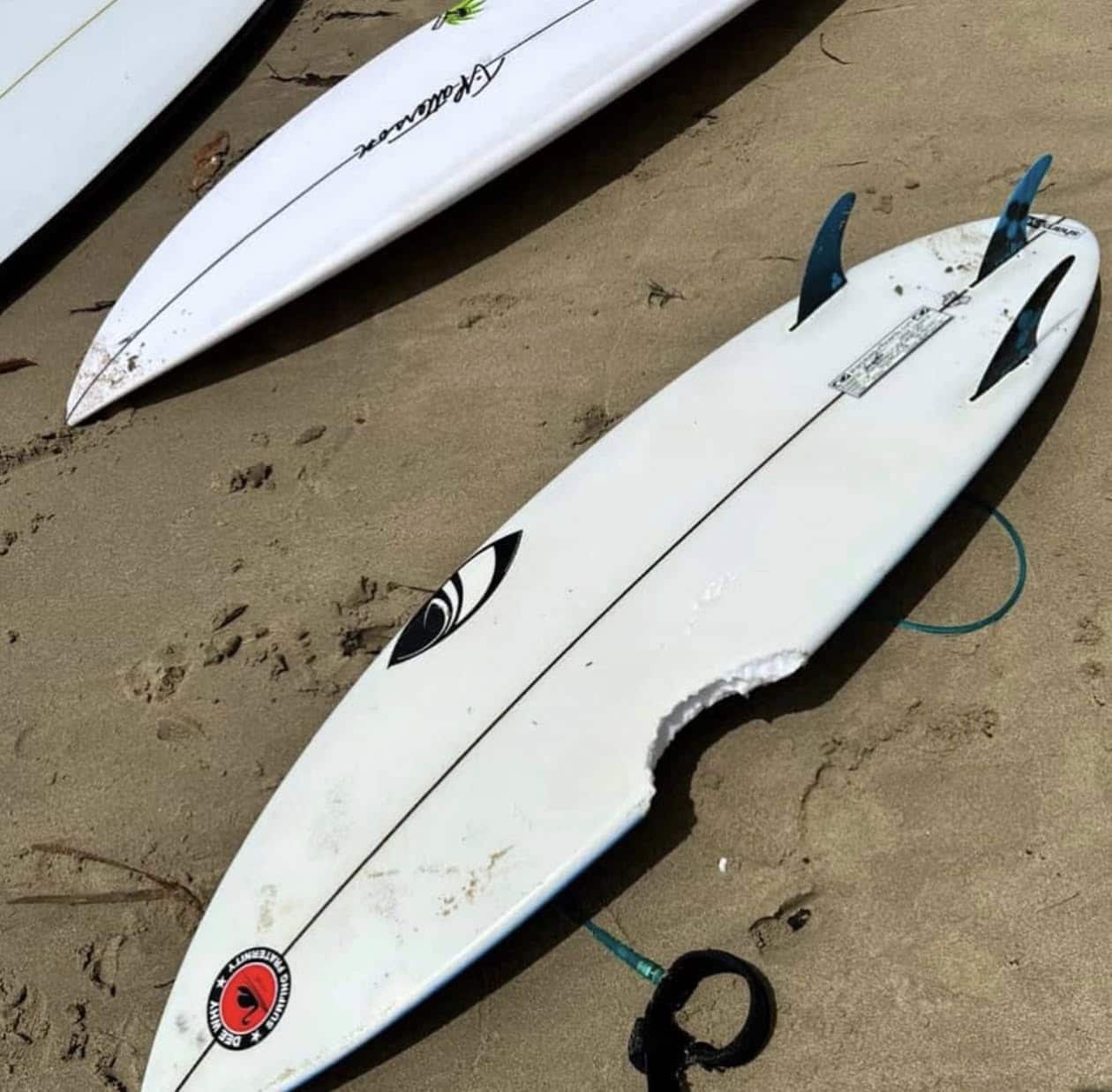 A white surfboard on sand. The board has a large bite-shaped hole on its side