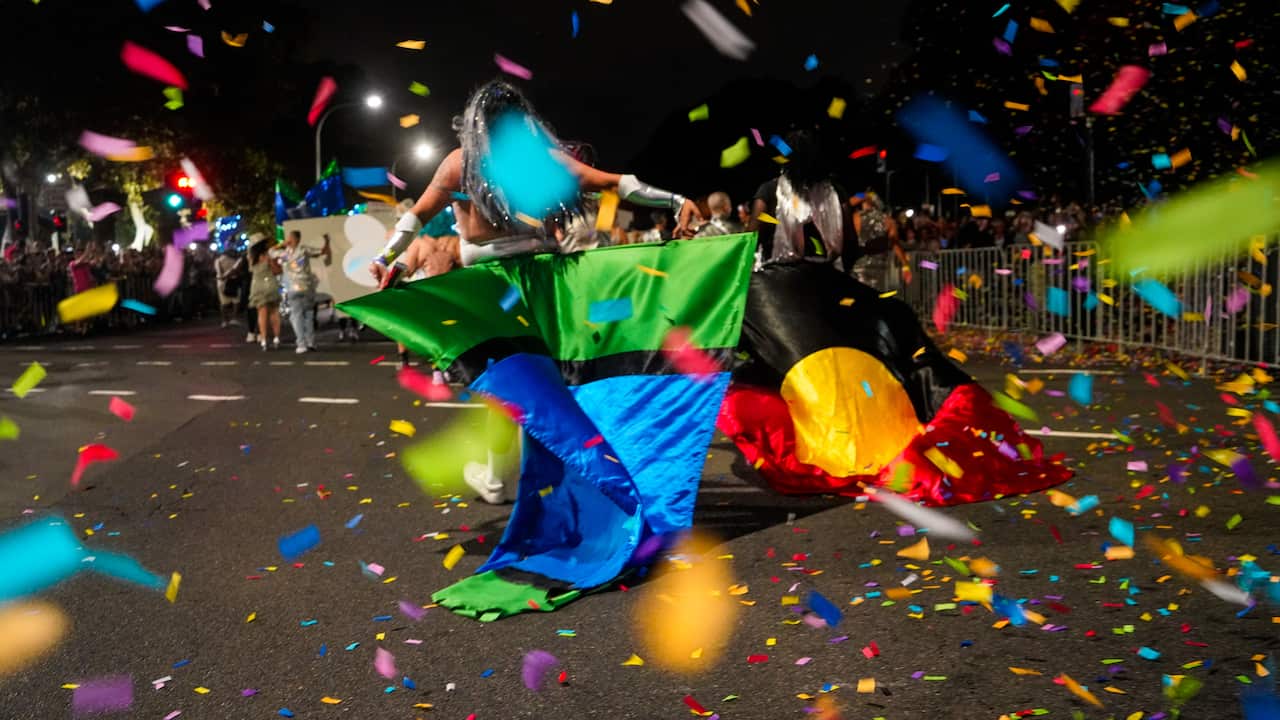 people walking in the mardi gras parade with an Aboriginal flag, and another green and blue flag; and glitter and confetti flies around in the air