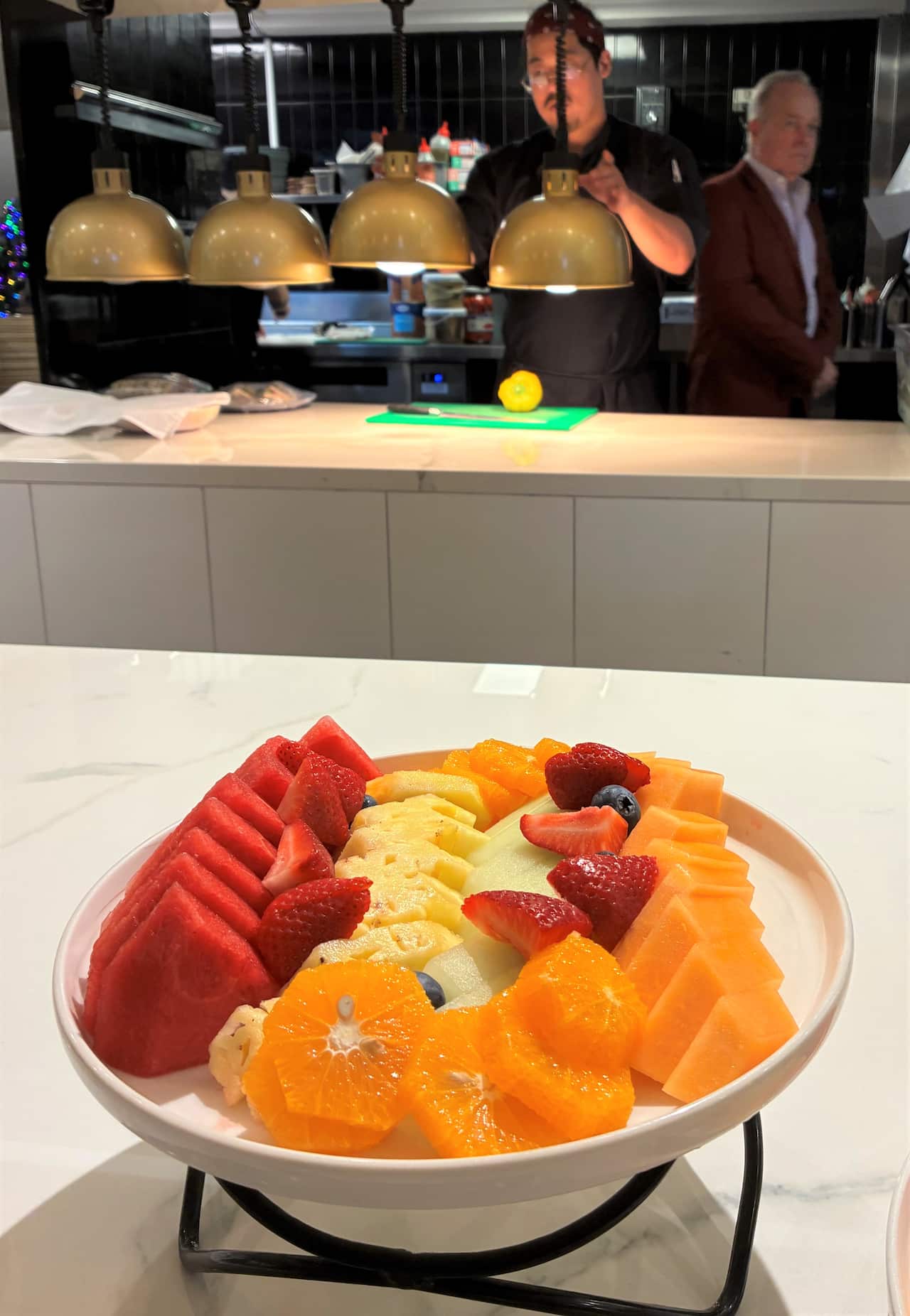 A bowl of diced fruit sits on a table in front of a commercial kitchen.