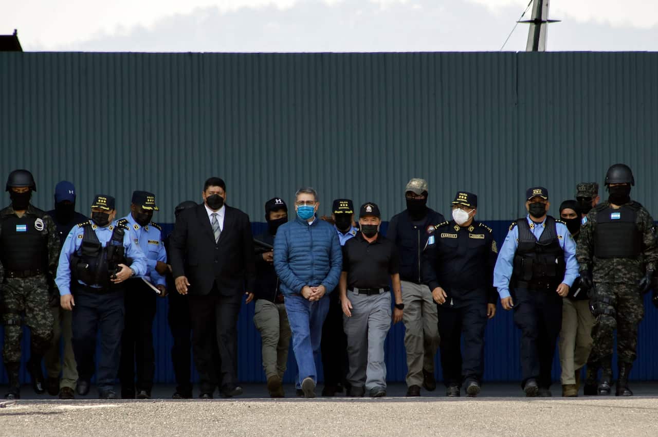 Former Honduran President Juan Orlando Hernandez, center, wearing a blue protective face mask and handcuffed, is escorted under heavy guard to a waiting aircraft at the Air Force base in Tegucigalpa, Honduras, Thursday, April 21, 2022.